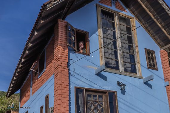 Mulher olhando pela janela de sua casa azul
