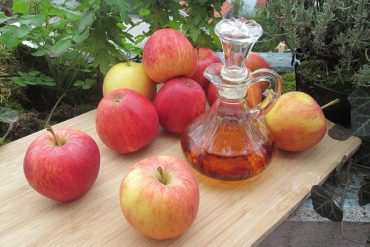Maçãs e um vidro contendo vinagre de maçã. sobre uma mesa de madeira