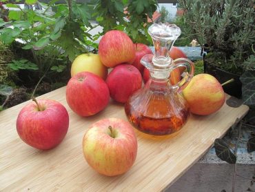 Maçãs e um vidro contendo vinagre de maçã. sobre uma mesa de madeira